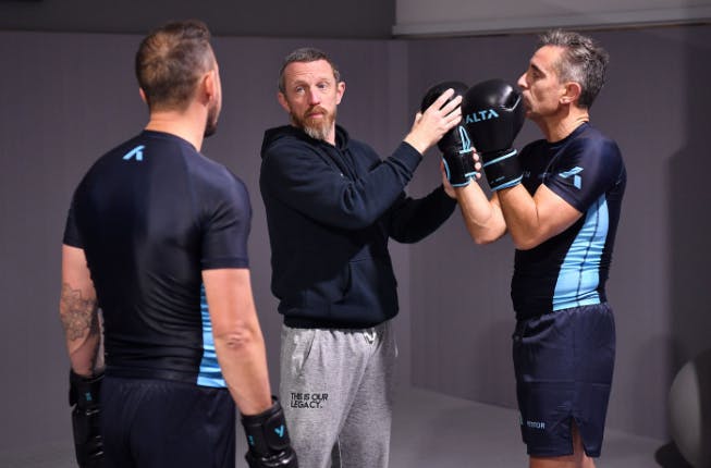 two men being taught boxing by coach at gym training 