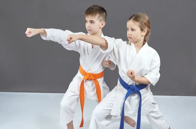 Two kids training martial arts wearing a traditional uniform and ranking belts